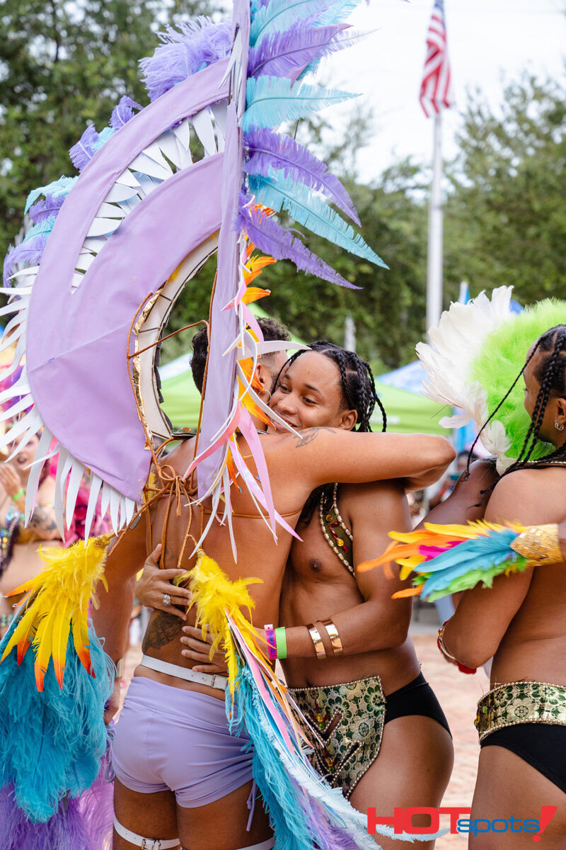 Two festival goers casually embrace while covered in feathers. Photo via Pridefete.lgbt