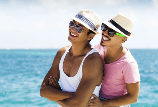 Cute couple smile and embrace in front of a shining, blue ocean. Photo via Shutterstock