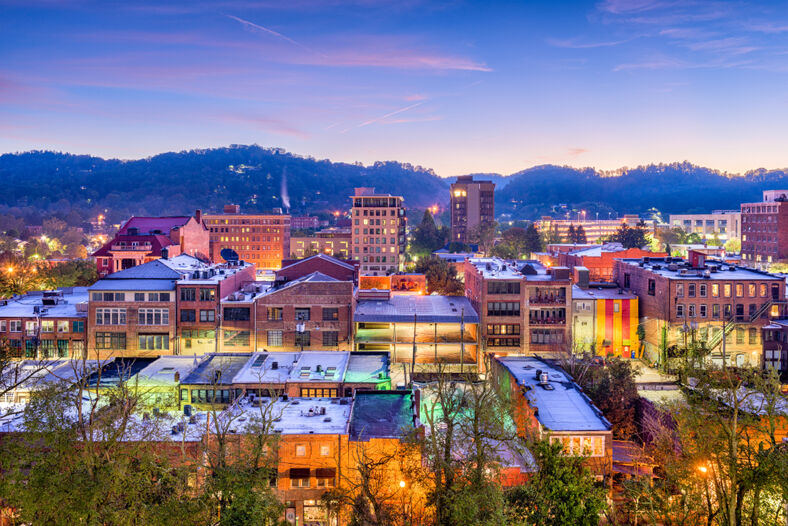 A view of Asheville, North Carolina's downtown skyline with the buildings awash in color during dusk.