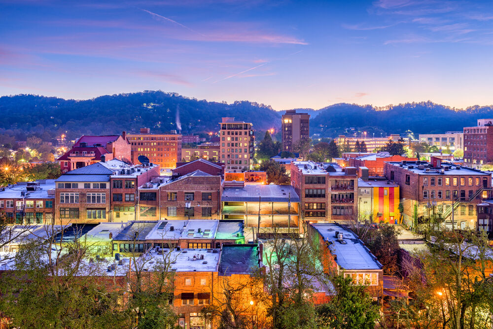A view of Asheville, North Carolina's downtown skyline with the buildings awash in color during dusk.