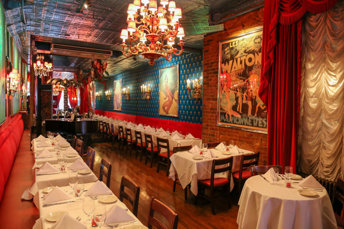 Inside of Chez Josephine main dining room with white table cloth, chandeliers, and posters of Josephine Baker. 