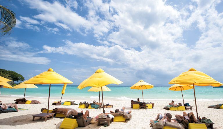 Yellow beach umbrellas shade people lounging on the sand looking out on turquoise waters