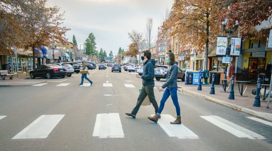 Two people cross the street of a busy and quaint downtown street