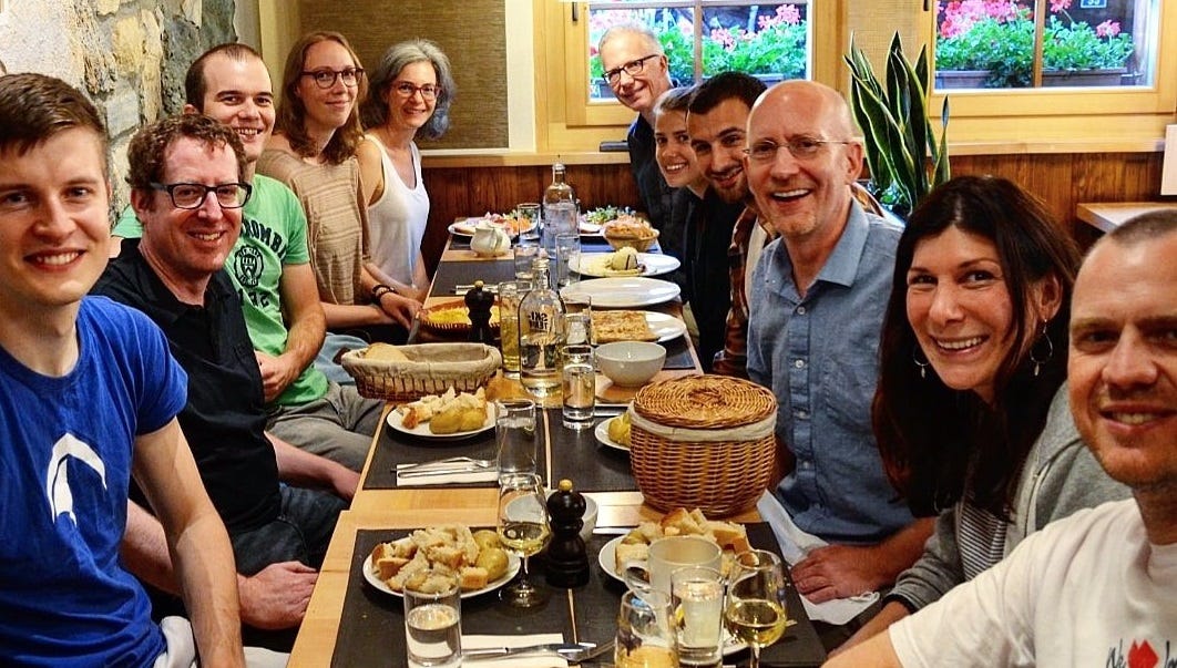 A crowd of people sit around a table eating fondue.