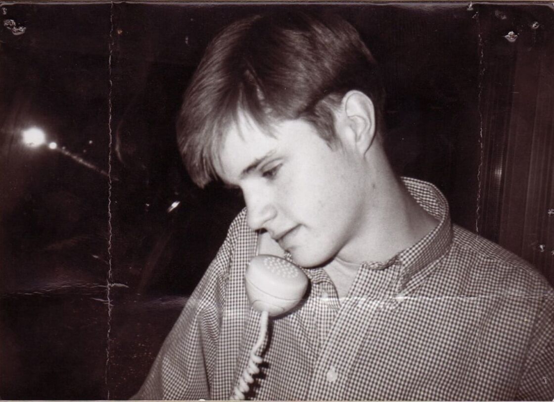 A black and white portrait of Matthew Shepard talking on a landline phone. 