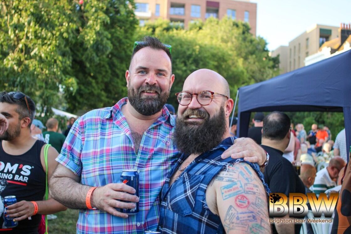 Two bearded men smile at the camera while standing outside at a festival