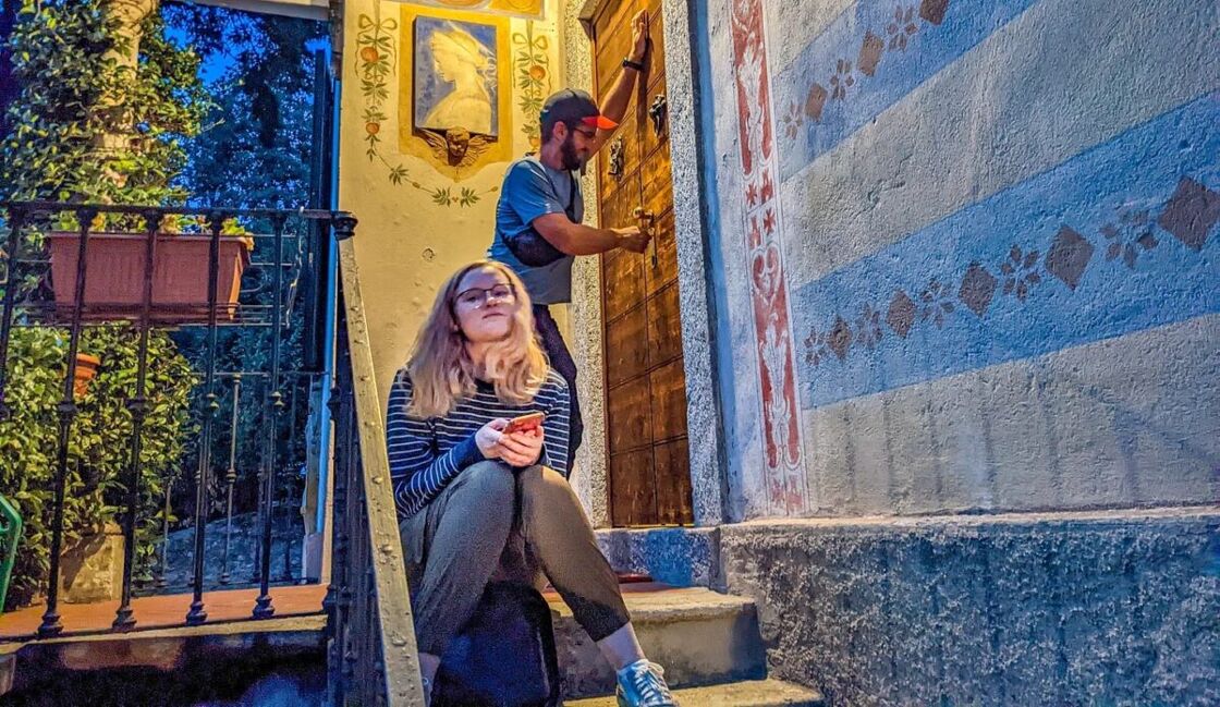 A woman sits on the steps outside of a villa while a man locks the door behind her