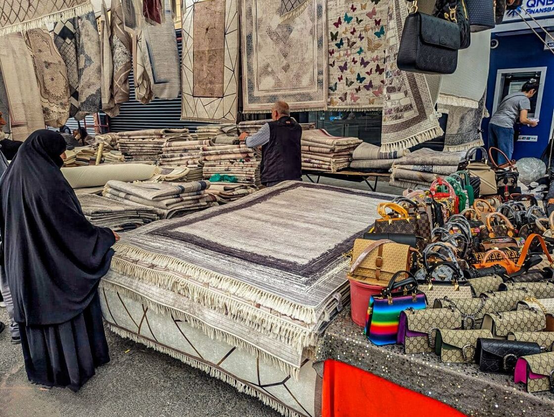 A woman dressed in a traditional black abaya looks at rugs. A Muslim woman looks at rugs in the marketplace
