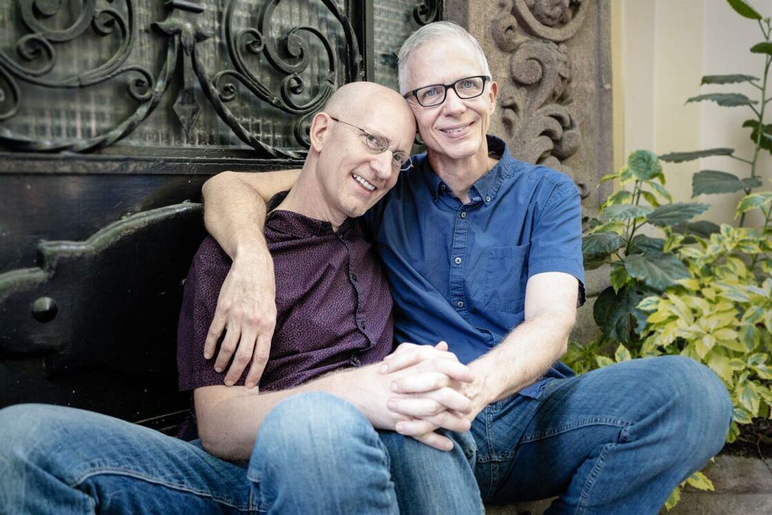 Brent Hartinger and Michael Jensen cuddle together on a bench outdoors.