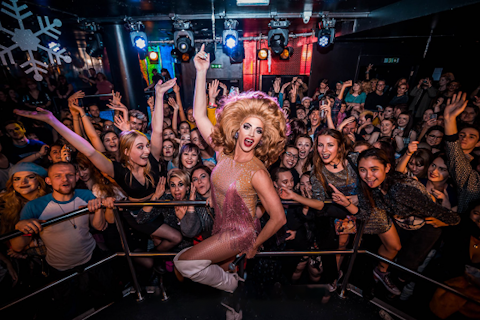 Drag queen stands in front of a waving crowd
