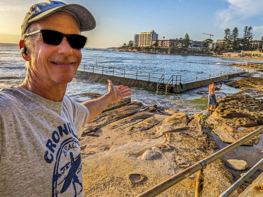 Michael gesturing at the rock pool behind him. Wearing a Cronulla t-shirt while visiting one of Cronulla’s rock pools.