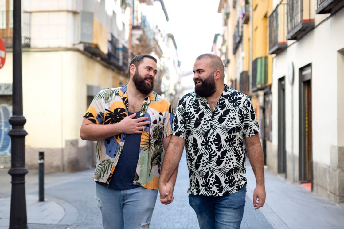 A gay couple wearing casual clothing walking together on a city street in a foreign country