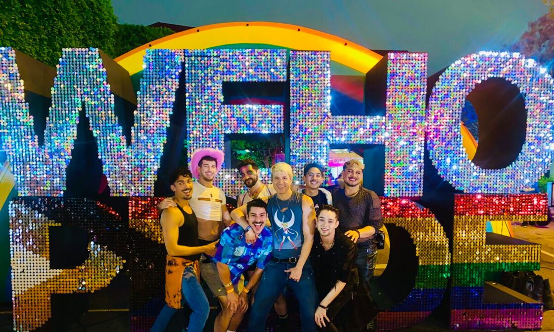 A gaggle of gays posing at the rainbow entrance of WeHo Pride.