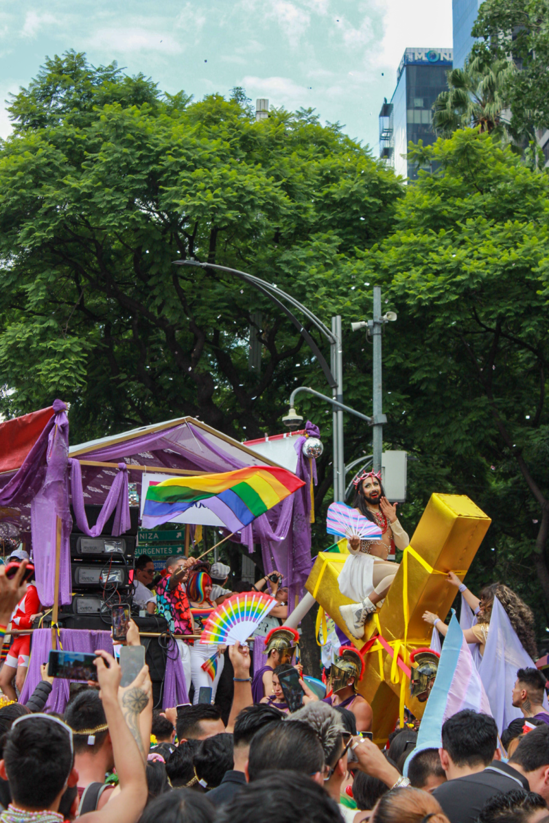 A drag queen dressed like Jesus rides a golden cross
