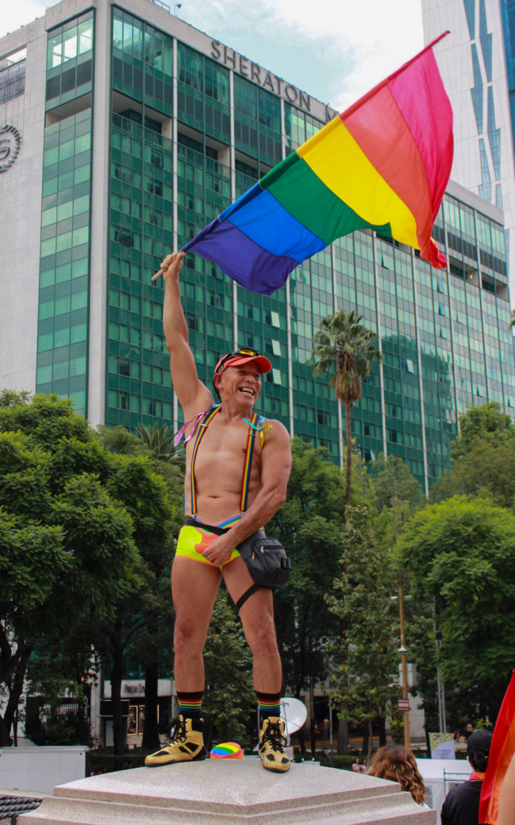 A man wearing yellow underwear waves the pride flag