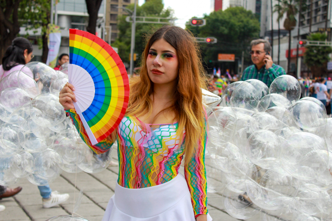 A young woman holding a rainbow fan poses in her costume made up of plastic bubbles