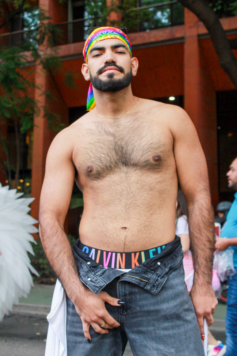 A young shirtless Latino man with a beard poses with his hand on his crotch