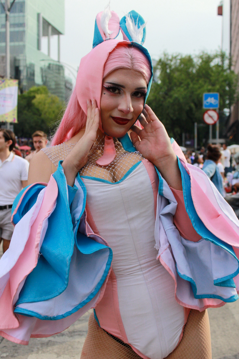 A trans woman stands on an outfit with the colors of the trans flag.