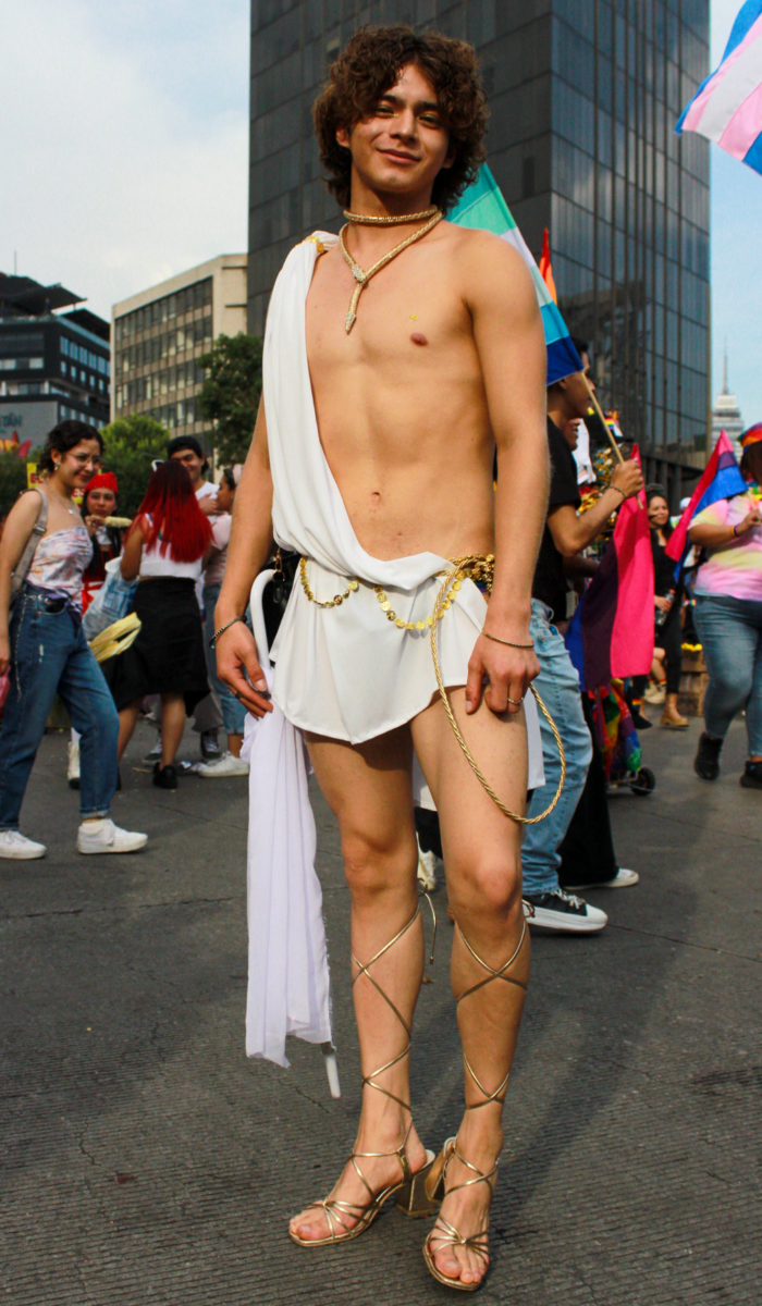 A young man with curly strikes a pose in a gold and white toga