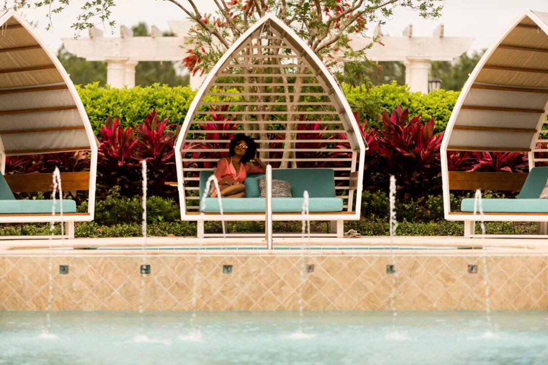 A woman sits in a luxurious private cabana next to a pool.