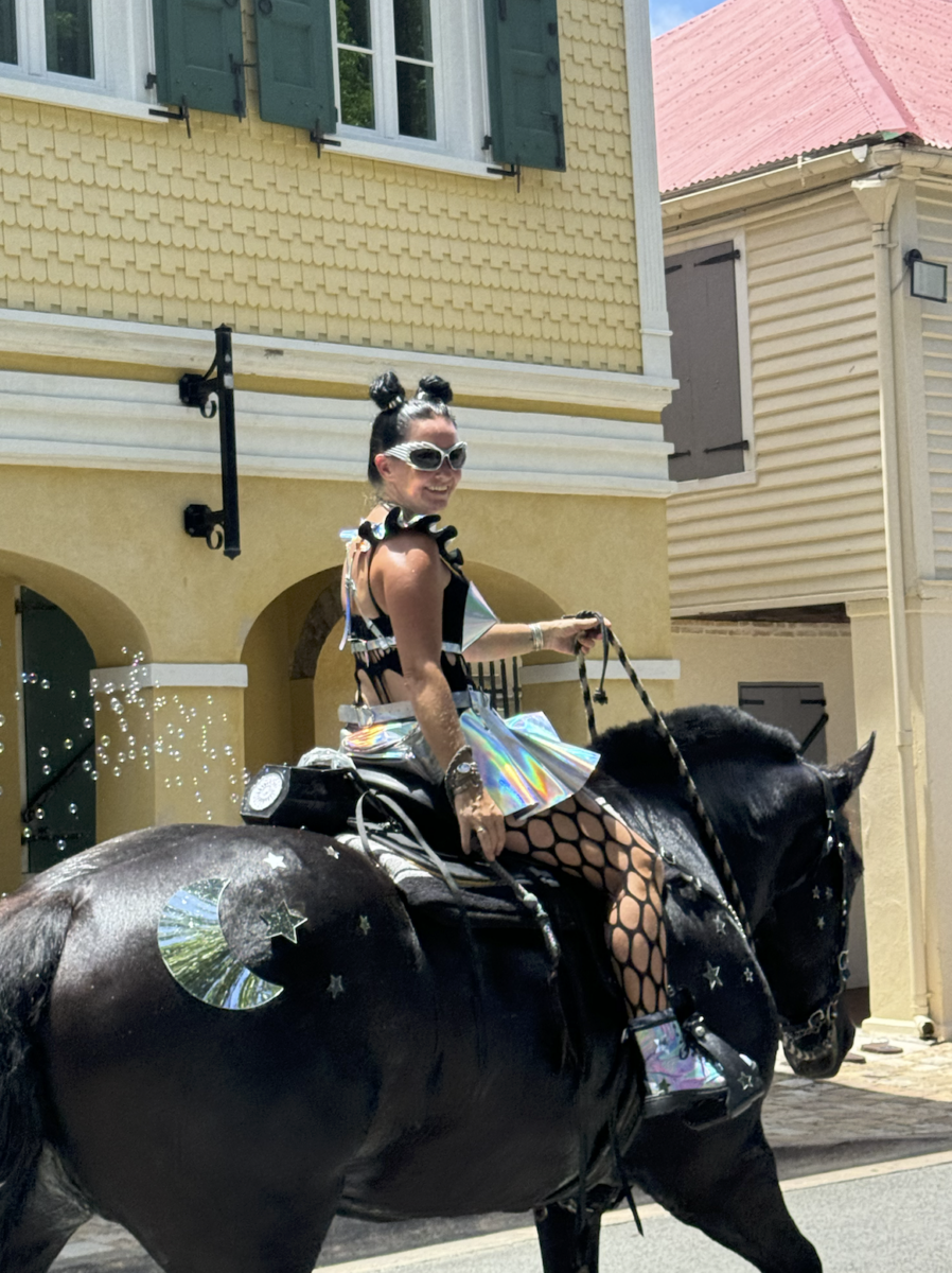 A Cruzean Cowgirl wearing a metallic skirt and metallic pinecones as a bra riding a horse. 