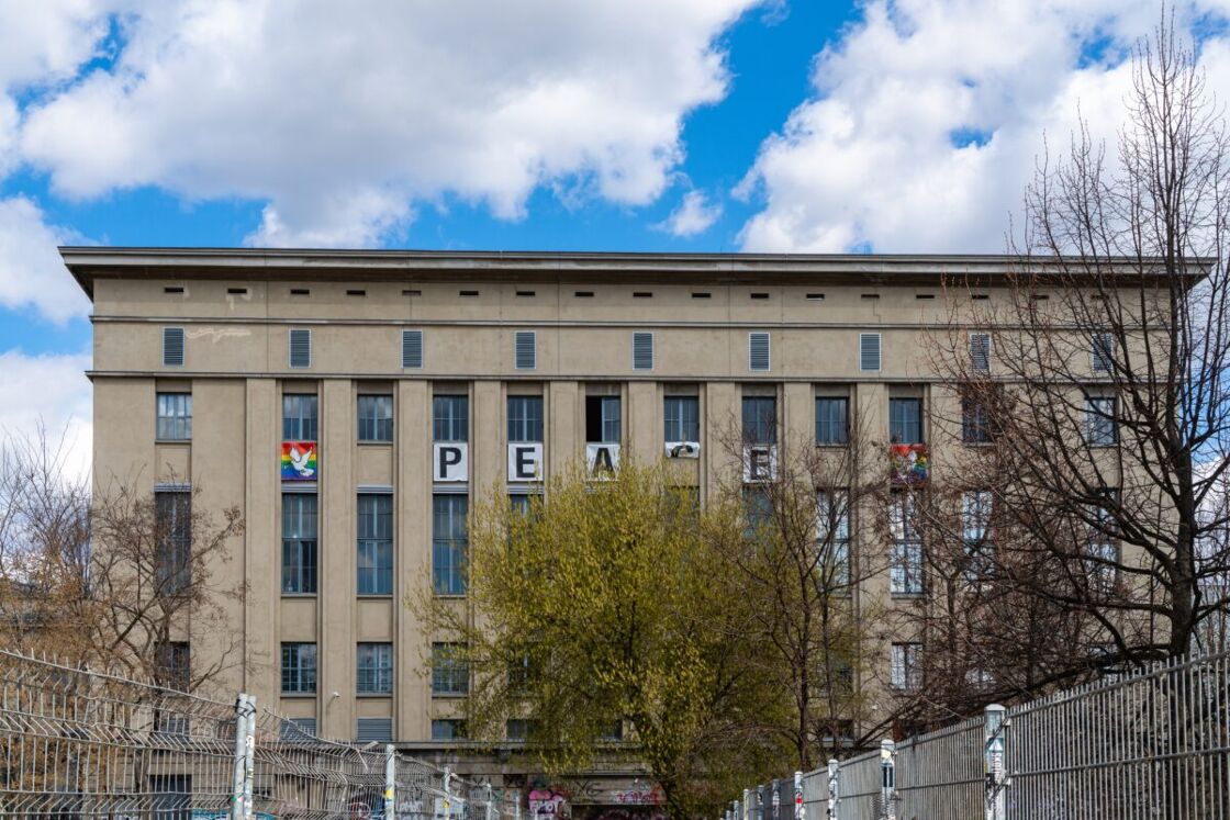 A landscape portrait of Berghain with rainbow flags and letters spelling out "PEACE" on the upper windows.