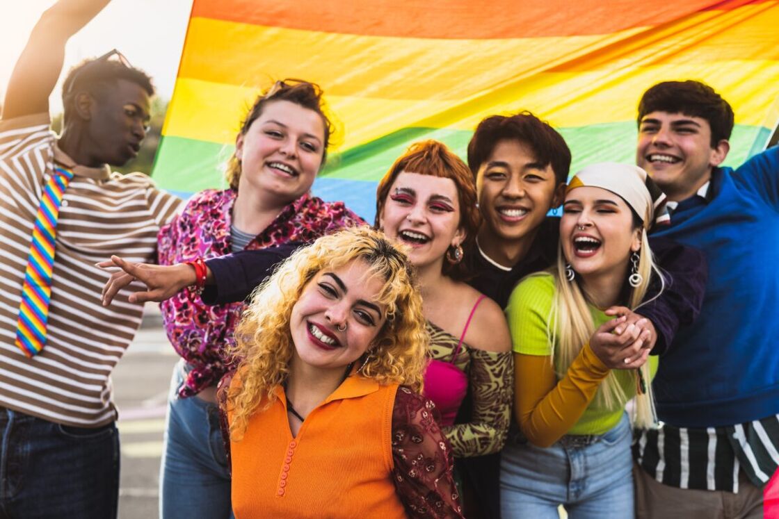 A group of queer youth waving a rainbow flag.
