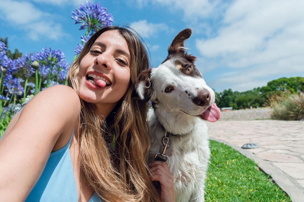 A young woman takes a selfie at a park with her dog