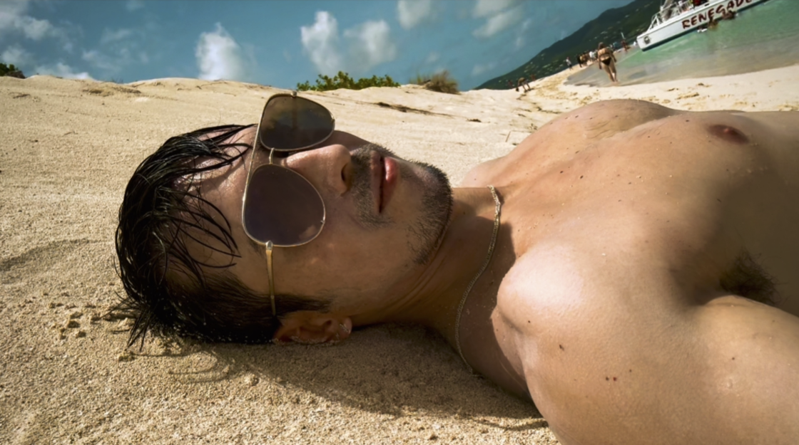 Photo of author shirtless with sunglasses lying on the beach at Buck Island.