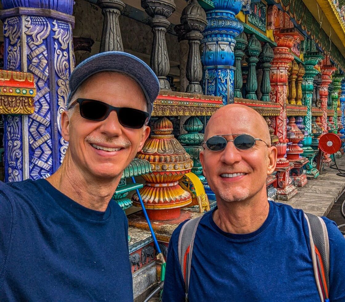 The author and his husband pose for a selfie in Malaysia against a color background of pottery and pillars