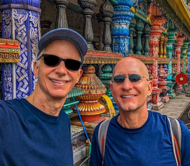 The author and his husband pose for a selfie in Malaysia against a color background of pottery and pillars