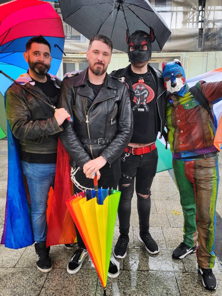 A group of men in leather jackets, two wearing puppy play masks