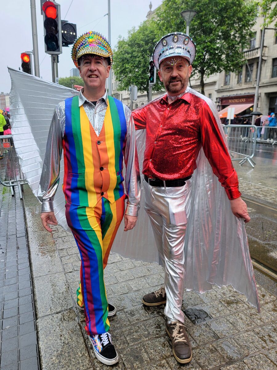 Two fabulously dressed men, one in a rainbow suit and the other with Silver Wings stand for the ccamera