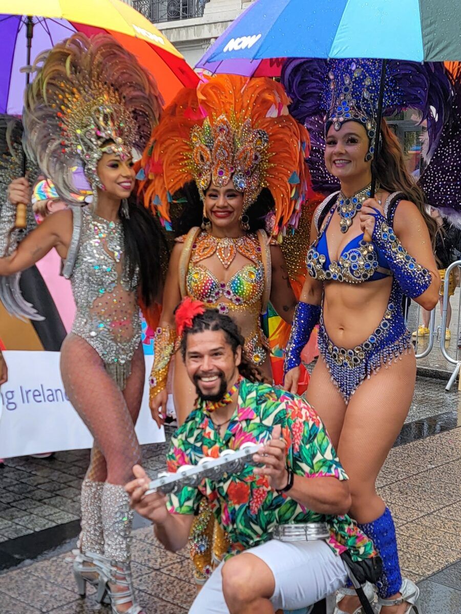 Women dressed in Rio Carnival outfits stand under umbrellas with a man in a bright shirt 