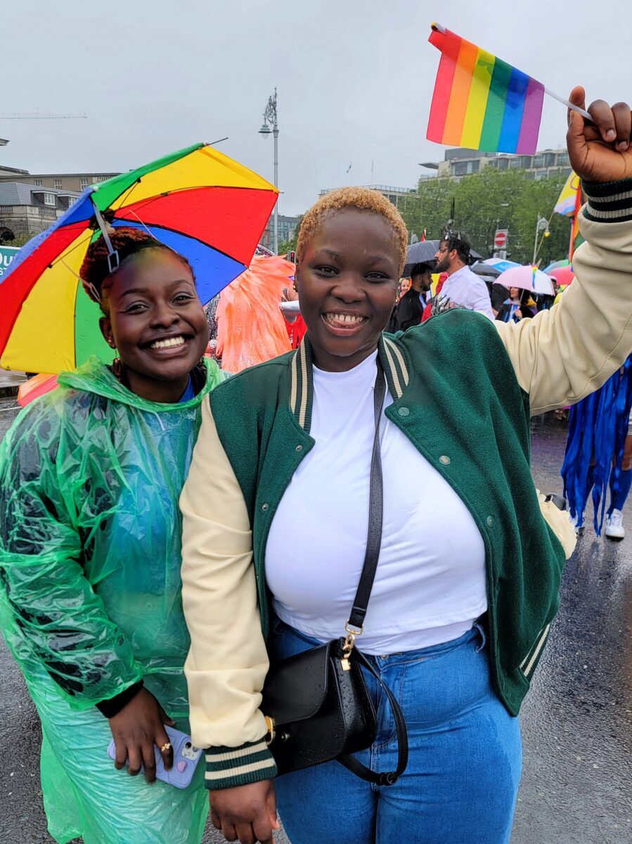 Two Black women smile and wave rainbow flags