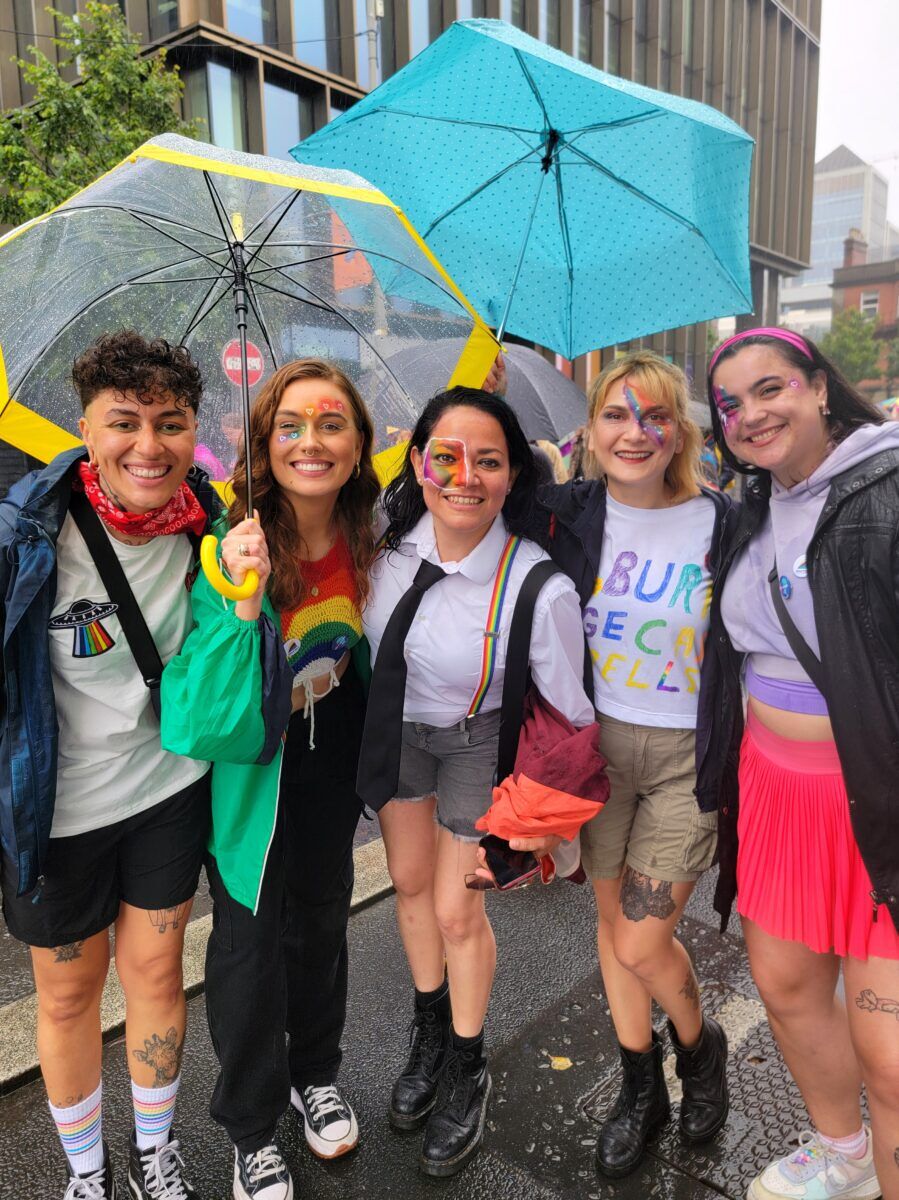 A group of young people standing and smiling under umbrellas