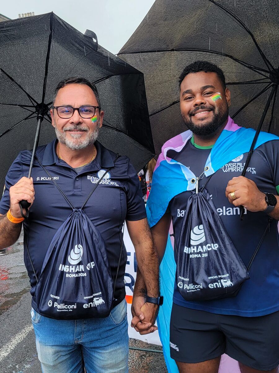 Two men stand under black umbrellas holding hands