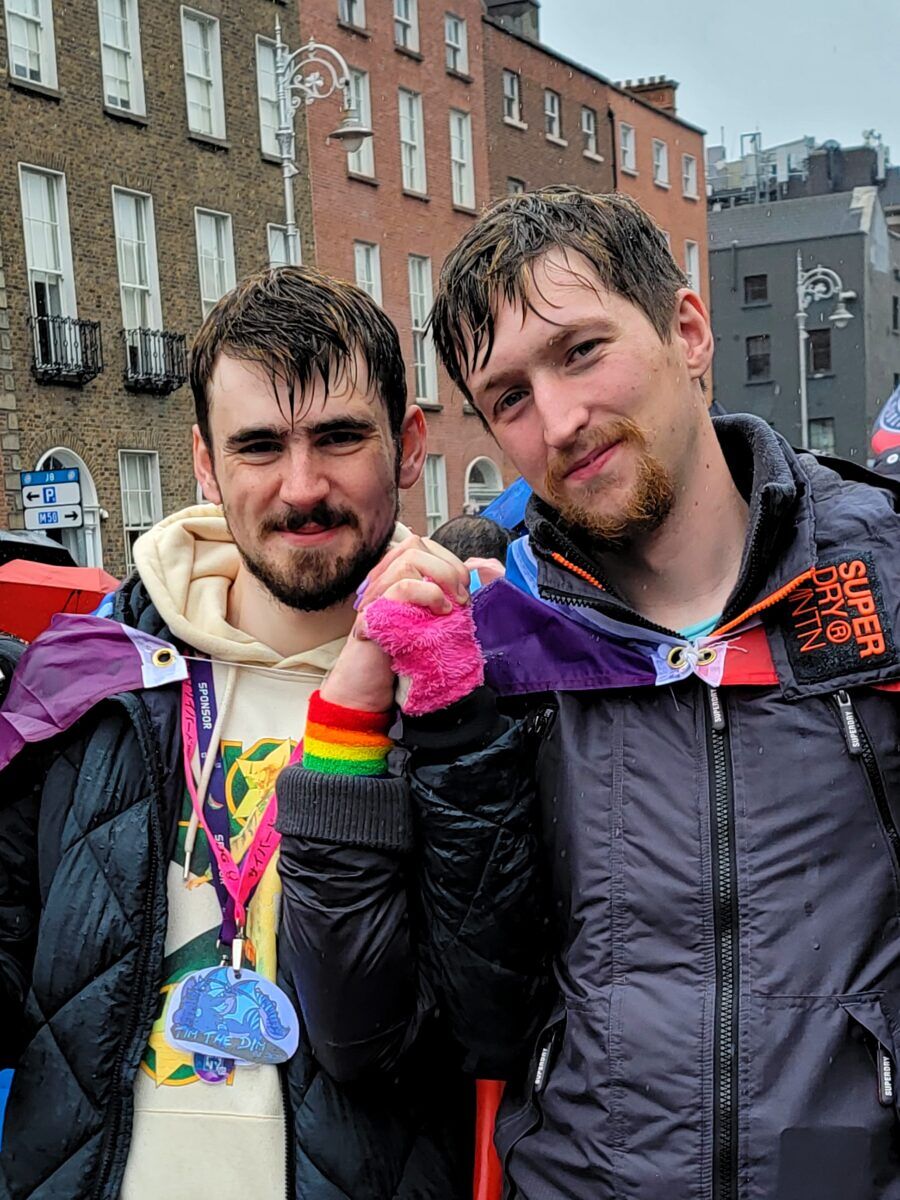 Two rain-soaked men stand hand in hand 