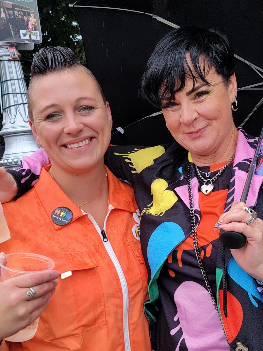 Two women with short dark hair stand together under an umbrella