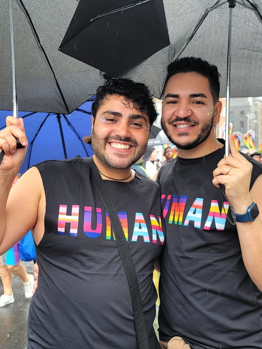 Two men wearing tanktops that say HUMAN in all colors of each LGBTQ+ flag