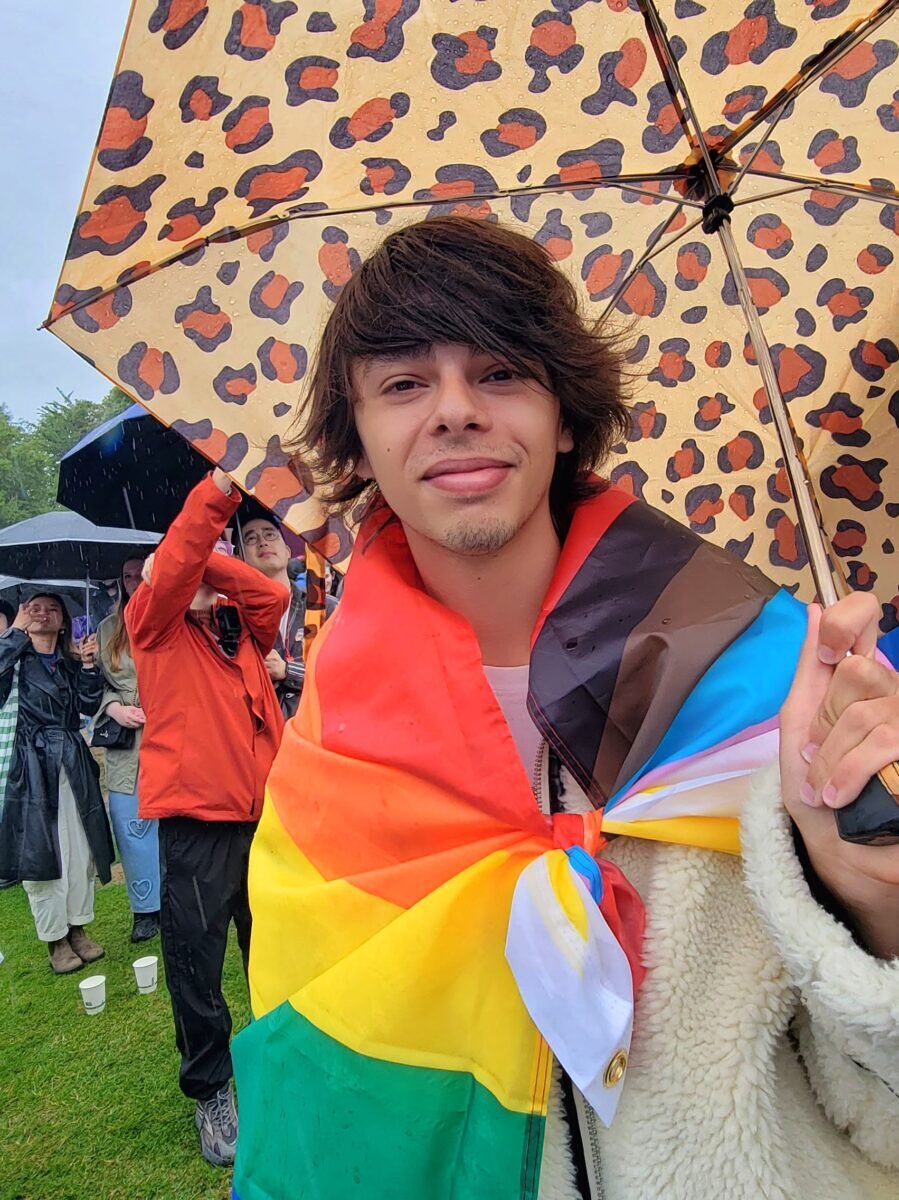 Young man wearing rainbow flag as a cape and holding a cheetah print umbrella