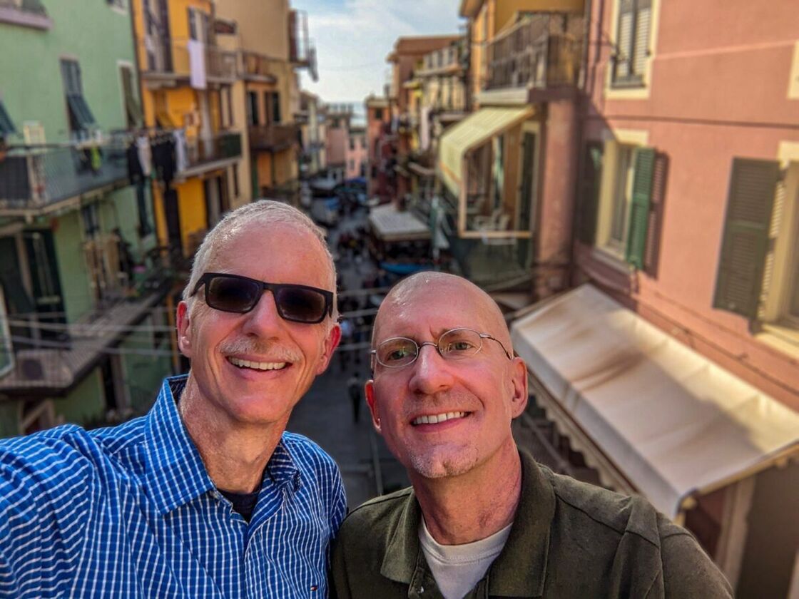 Michael and Brent in Italy. The author and his husband pose for a selfie in Italy with a street behind them