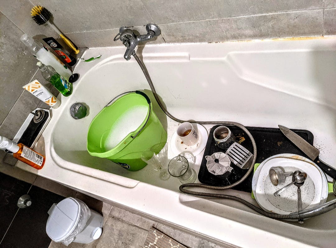 Dishes and a bucket of soapy water sit inside of a bathtub