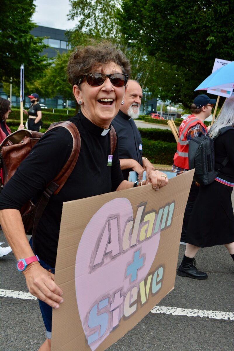 A woman holds a homemade sign that reads "Adam + Steve"