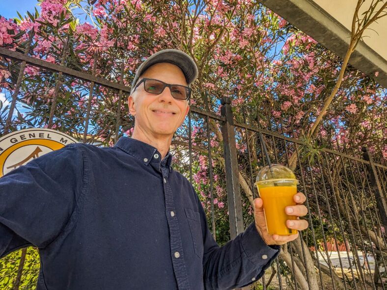 The author stands in front of a flowering tree holding a glass of orange juice