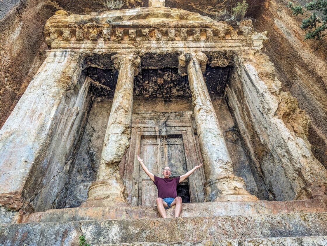 Brent Hartinger poses with outspread arms in front of a Lycian tomb's entrance