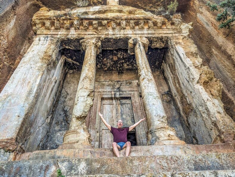 Brent Hartinger poses with outspread arms in front of a Lycian tomb's entrance