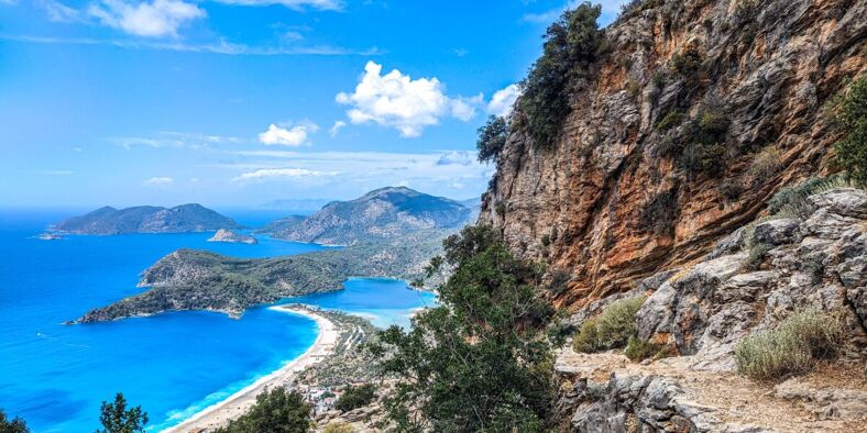 A view of a rocky coastline with a turquoise blue sea and mountains in the background