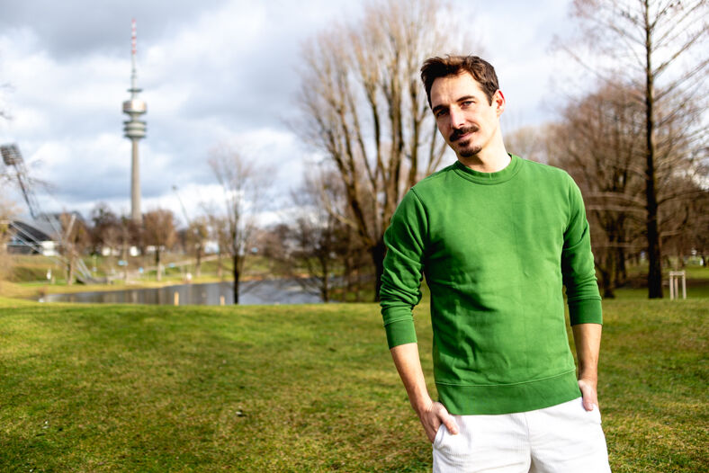 A man wearing a green sweater poses in a park