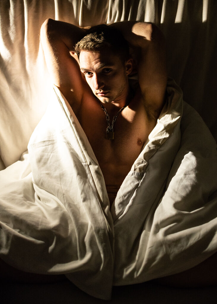 A man poses in a bad wrapped in a comforter